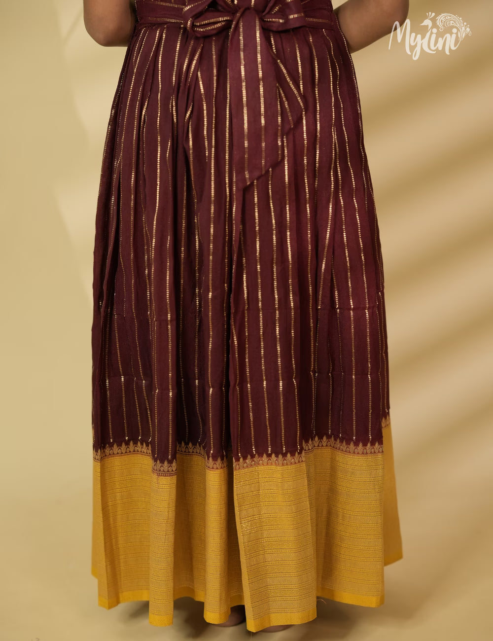 Young girl in a maroon and yellow traditional outfit holding dried leaves against a beige background