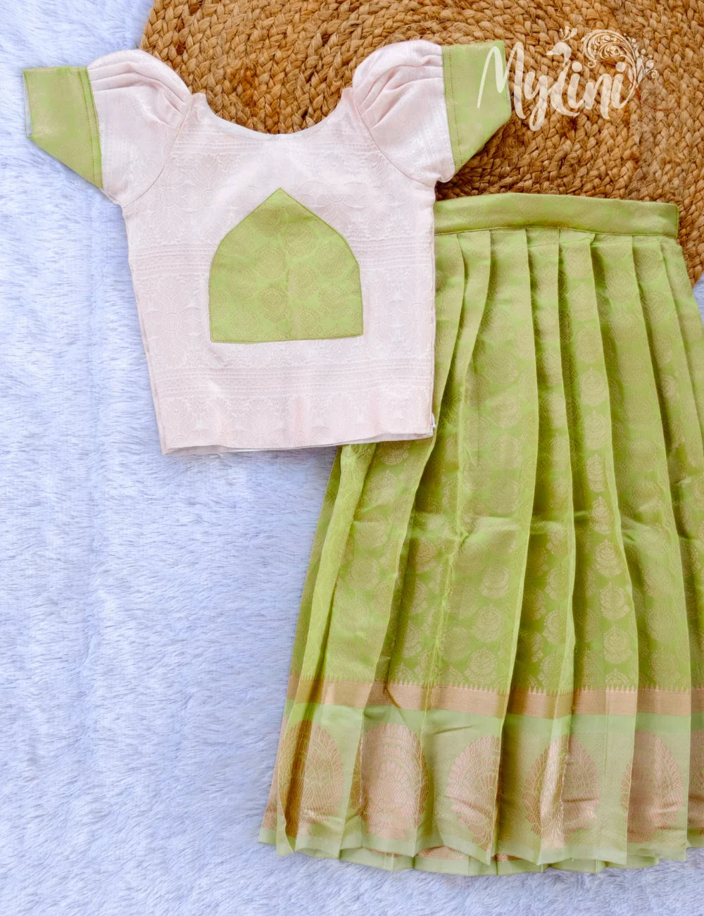 Young girl wearing a white top with green accents and a green skirt on a beige background