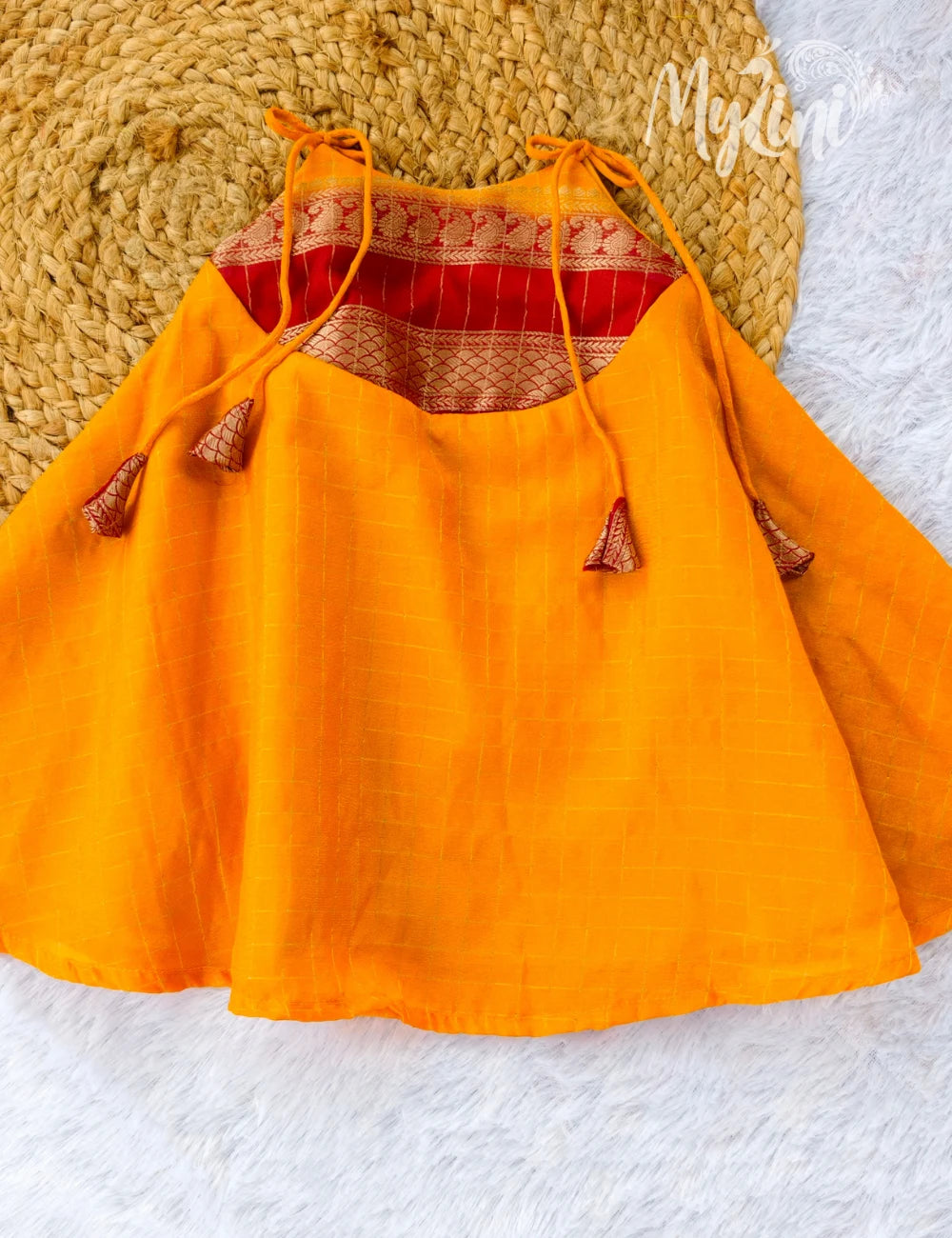 Baby in an orange dress with red accents sitting on a white surface.