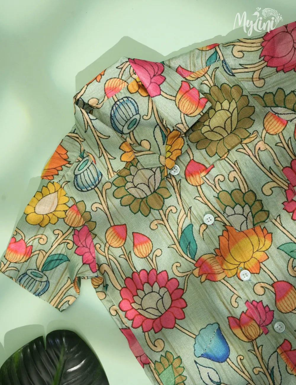 Child wearing a floral shirt and beige shorts standing against a beige background with plants.