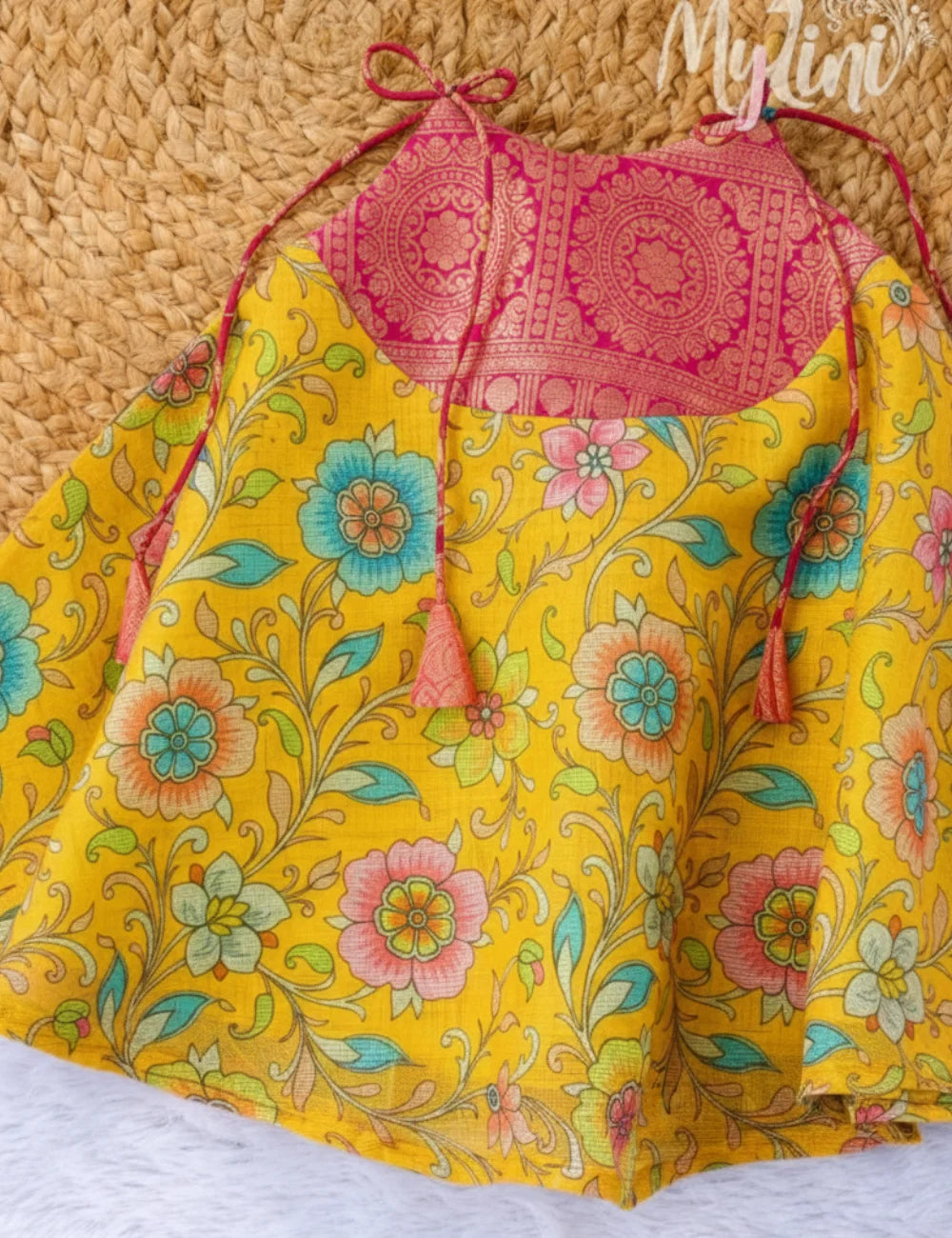 Baby wearing a pink top and yellow floral dress with a neutral background