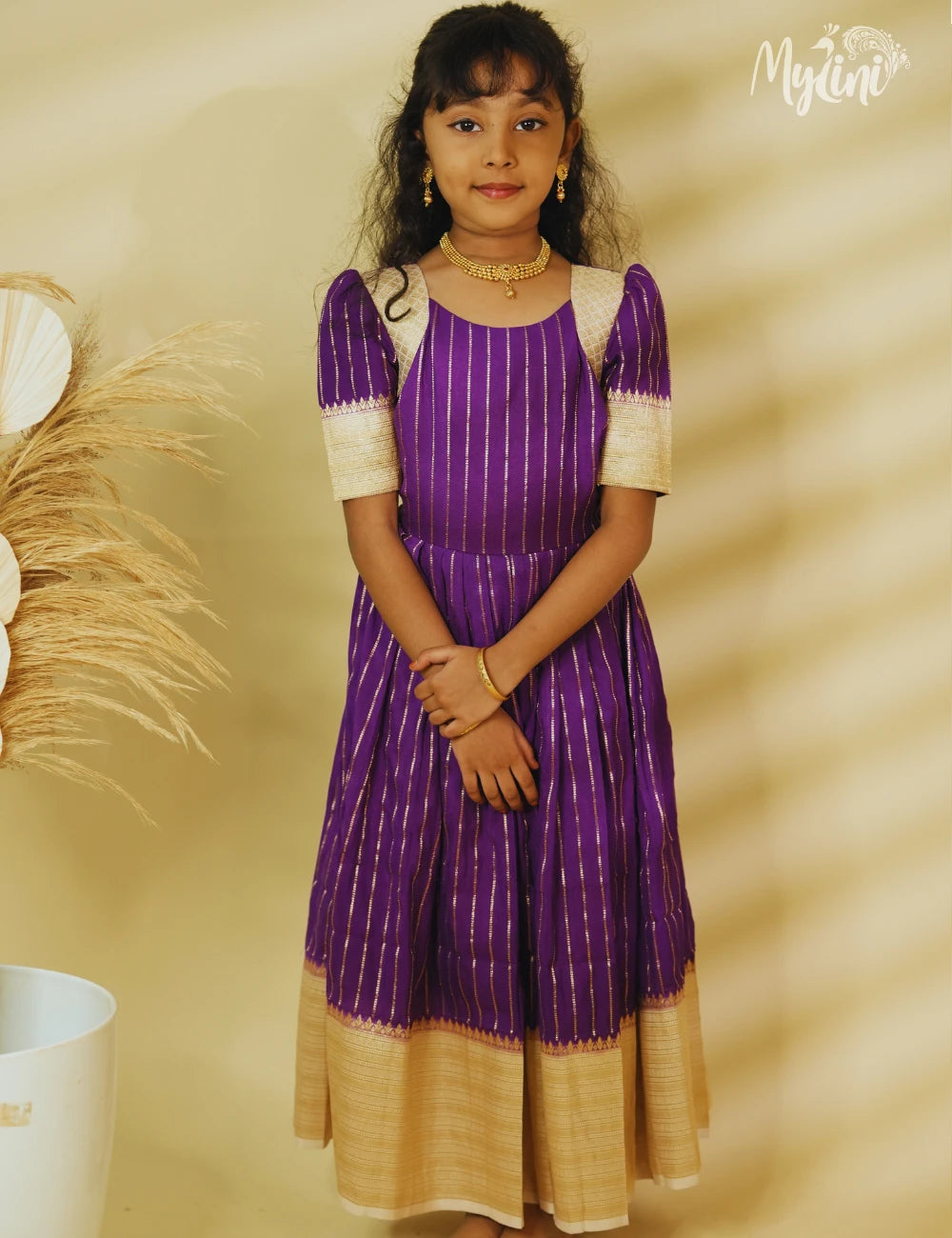 Child wearing a purple and gold traditional dress against a beige background