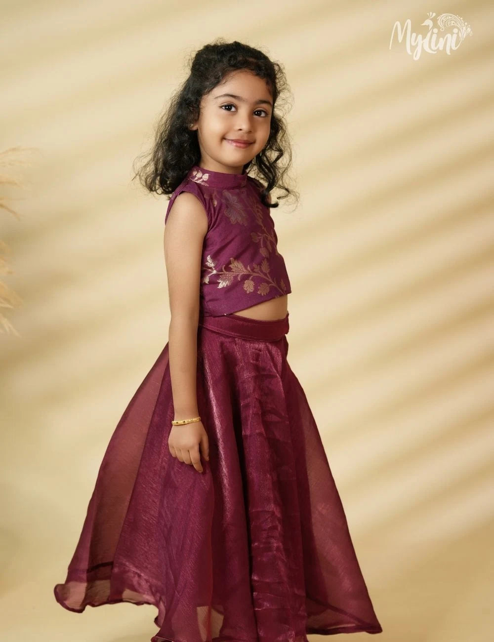 Young girl wearing a maroon traditional outfit with floral embroidery on a beige background