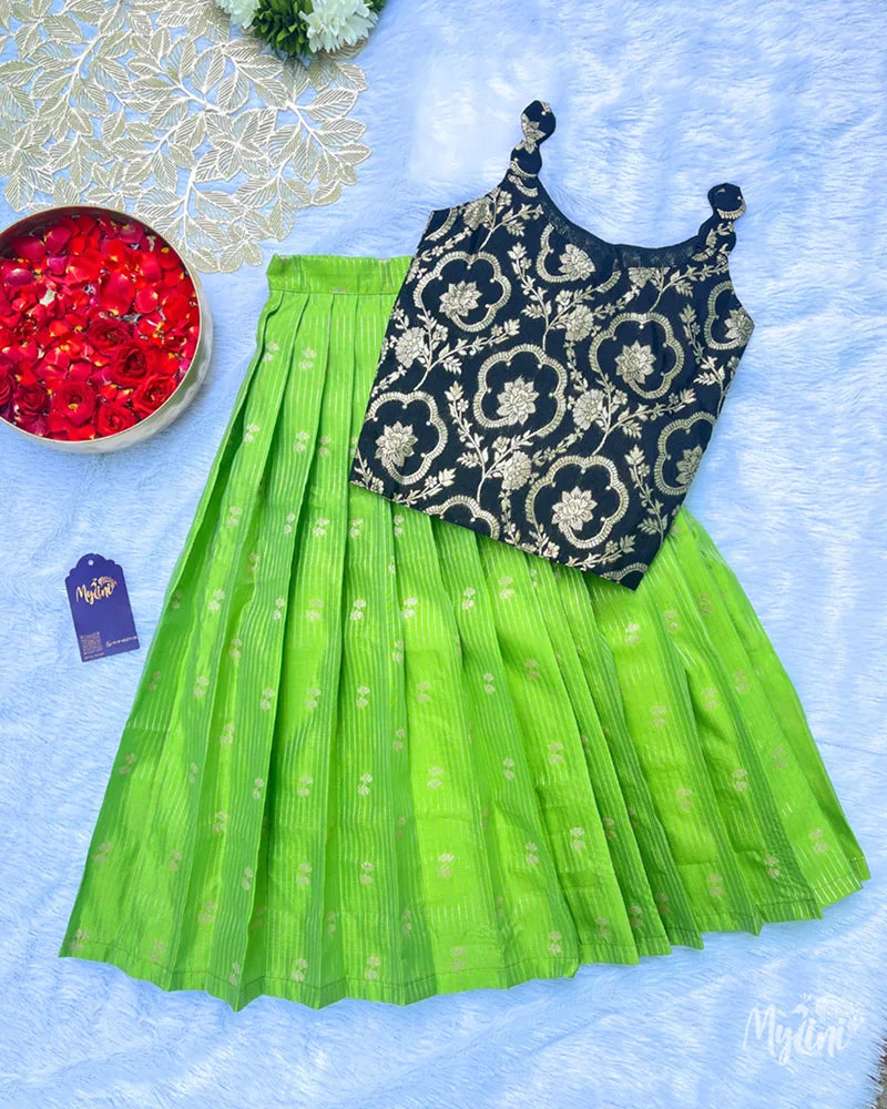 Young girl in a black floral top and green skirt standing indoors with decorative background