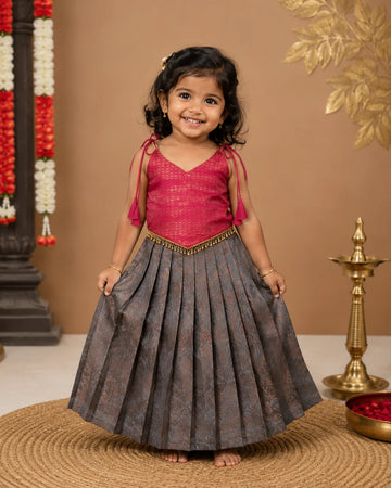 Young girl in a red top and gray skirt standing on a woven mat with decorative background