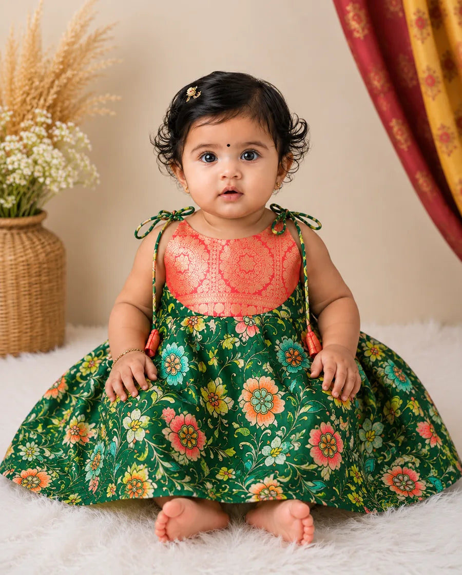 Baby wearing a floral dress with a pink top, sitting on a white surface with a neutral background.