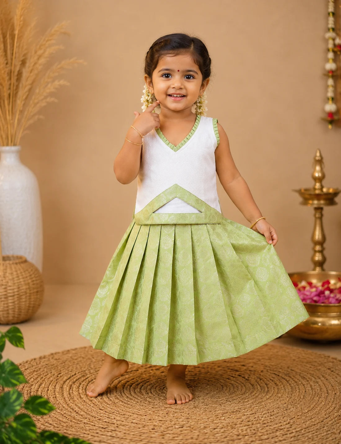 Young girl in a white and green traditional outfit standing on a woven mat with a beige background.