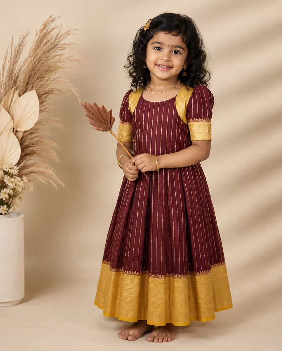 Young girl in a maroon and yellow traditional outfit holding dried leaves against a beige background