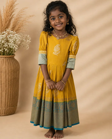 Young girl in a yellow dress with green accents standing against a beige background