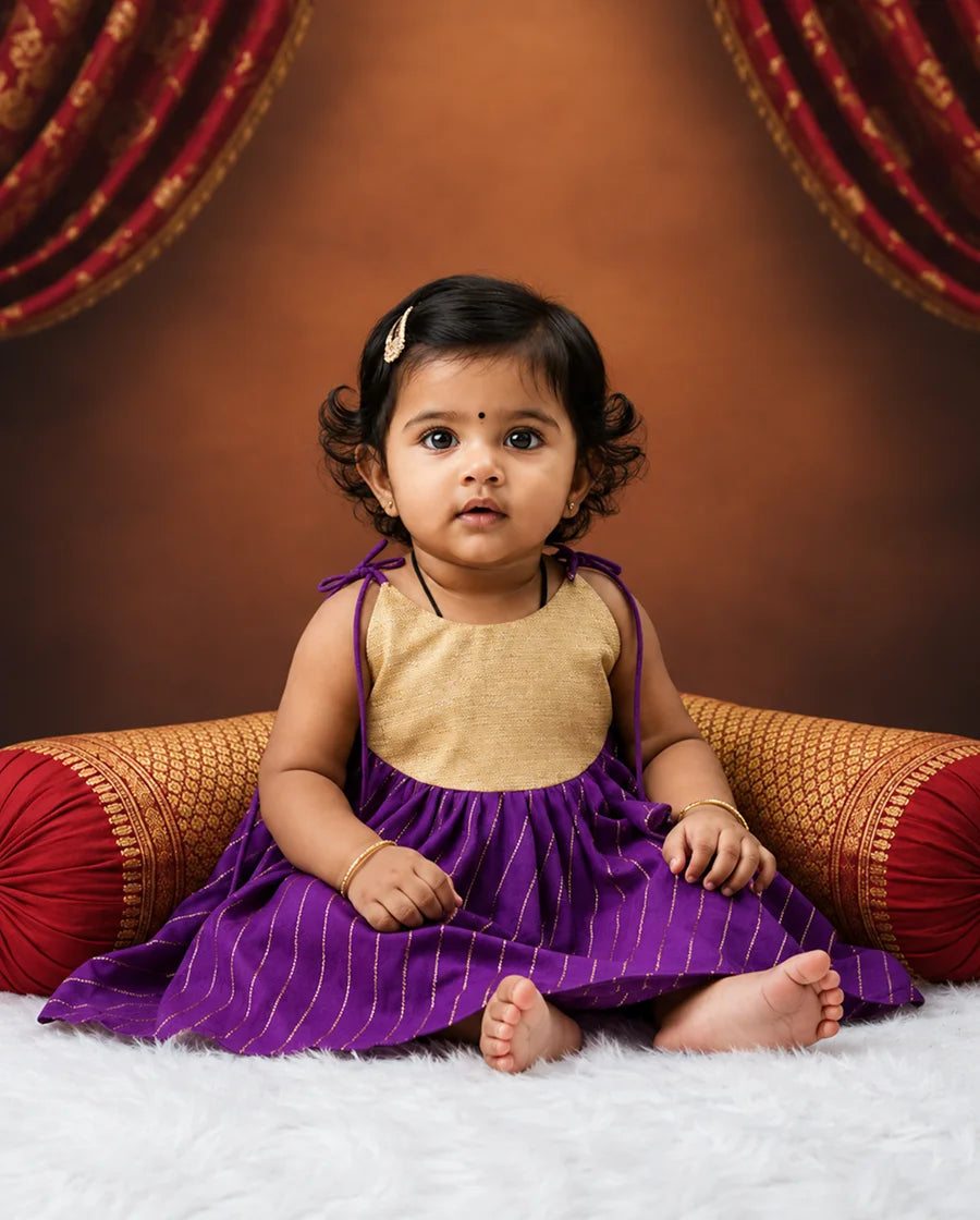 Child wearing a purple and gold outfit sitting on a decorated couch.