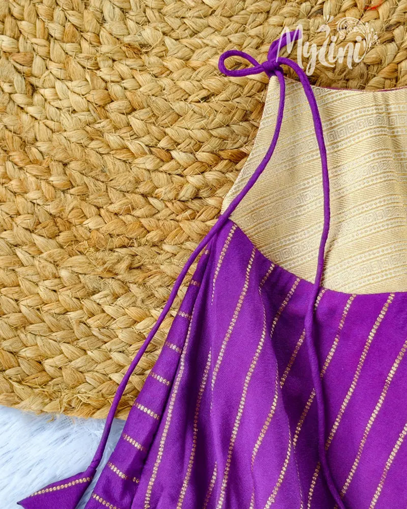 Child wearing a purple and gold outfit sitting on a decorated couch.