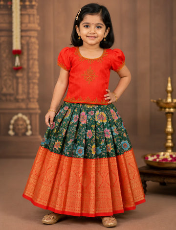 Young girl wearing a traditional outfit with a red top and colorful skirt against a decorative background.