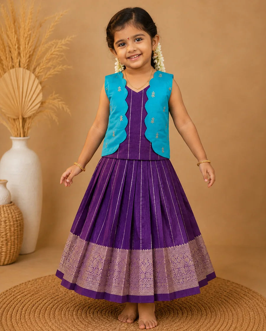 Young girl in a purple dress with a blue vest standing on a woven mat against a beige background.