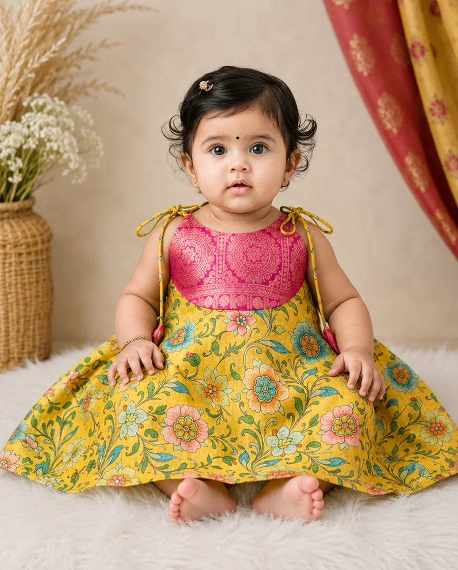 Baby wearing a pink top and yellow floral dress with a neutral background